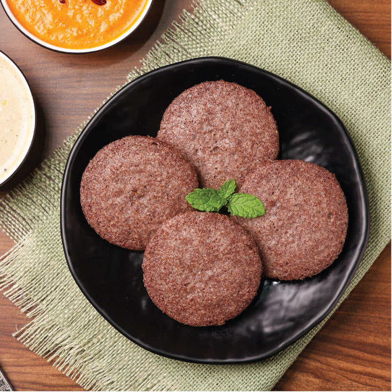 Four ragi idlis on a black plate, rich in nutrients and fiber